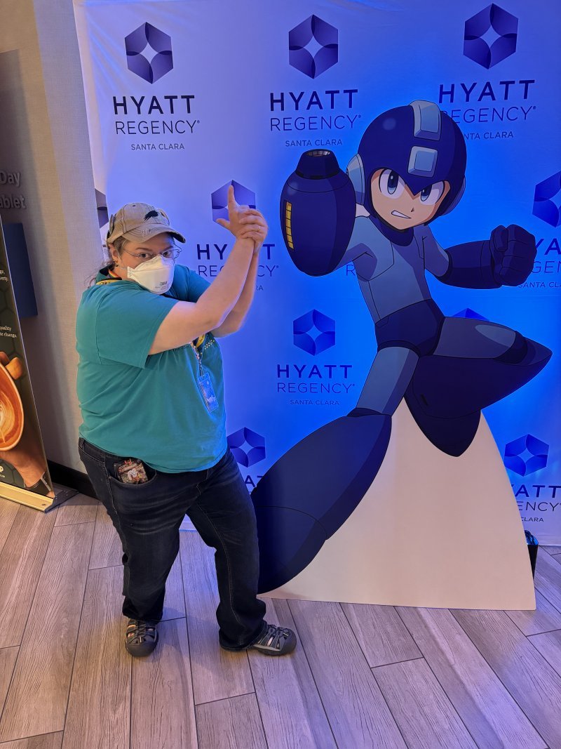 An artist posing next to a standee of Megaman at the Hyatt Regency Santa Clara hotel lobby.